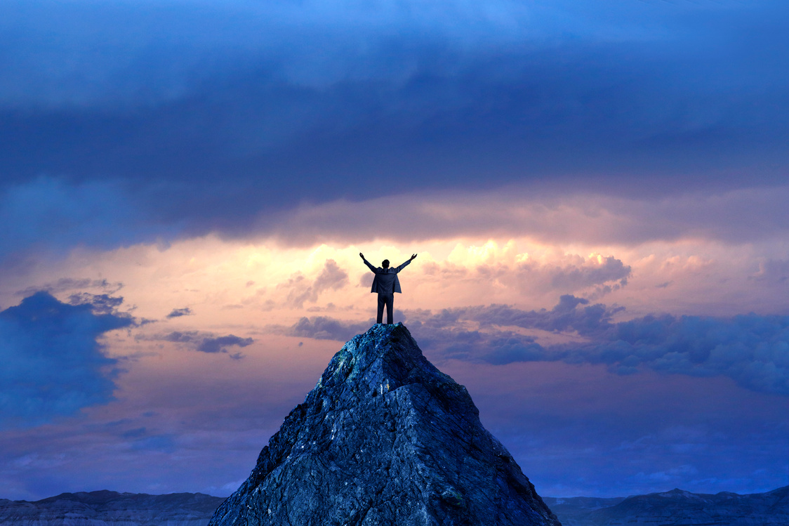 Businessman Standing On Mountain Peak